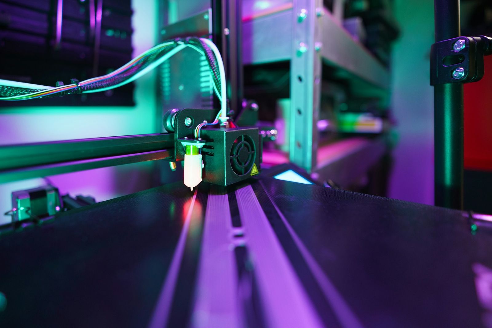 A 3D printer print head and gantry in purple and green light