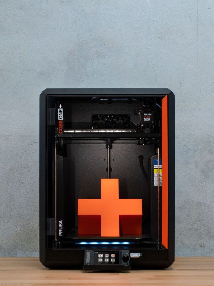 Prusa Core One 3D printer in front of a concrete wall