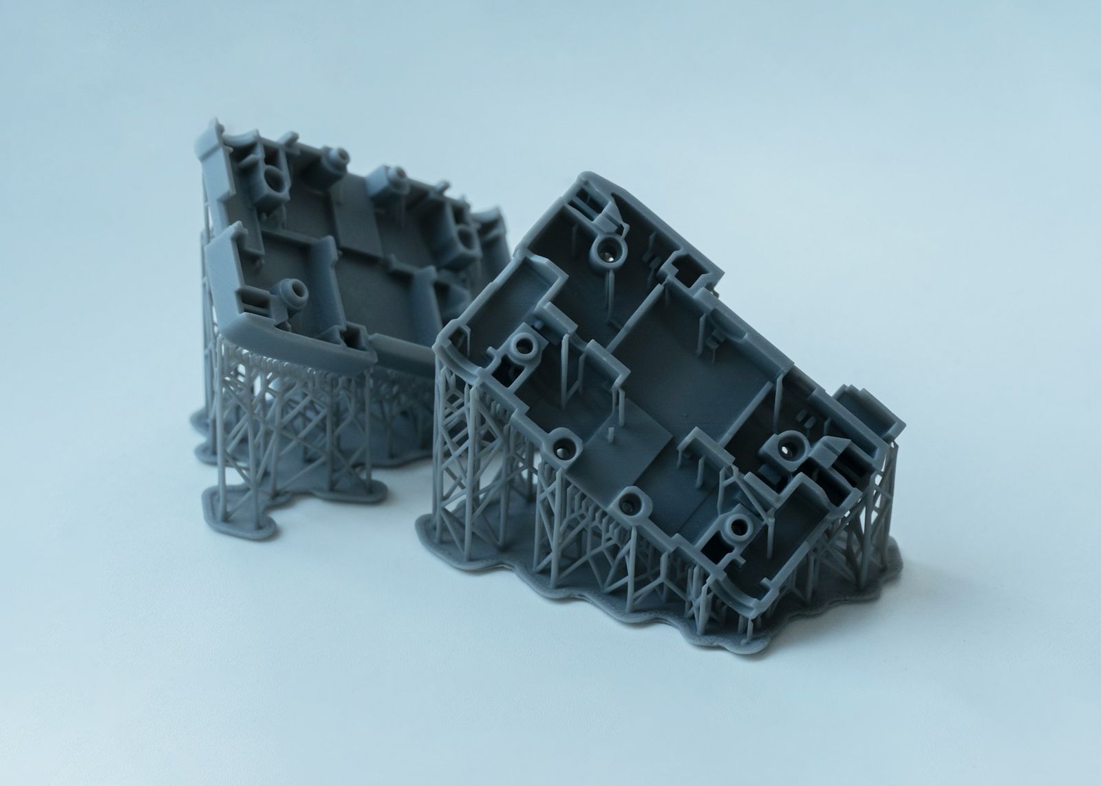 Two grey resin-printed parts still standing on their thin supports