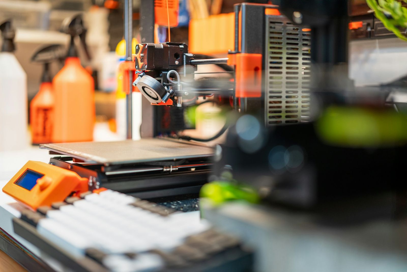 A filament 3D printer with orange parts on a workbench